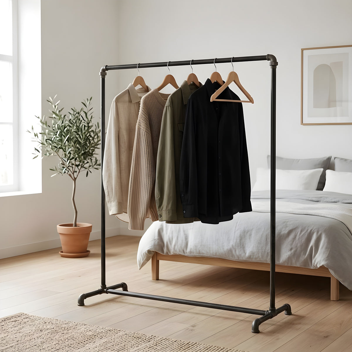 Arara de roupa industrial em tubos de canalização pretos num quarto luminoso, roupa em cabides de madeira