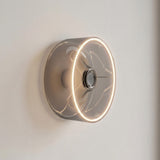 Lâmpada LED donut E27 em vidro fumado, Ø 195 mm, acesa como aplique de parede numa parede clara e sóbria