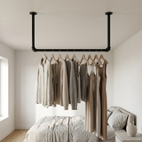 Varão de roupa suspenso do teto em tubo preto num quarto, roupa em cabides de madeira